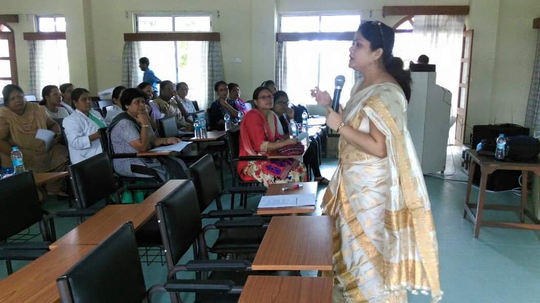Atifa Deshamukhya addressing participants with a microphone during a classroom training session.