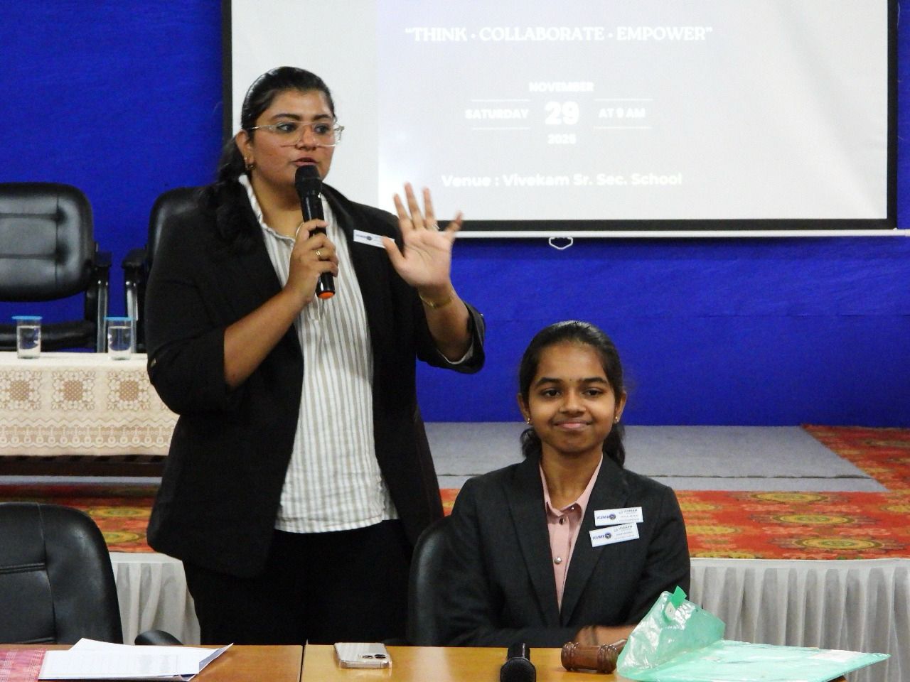 Frishthaa Dawulath speaking into a microphone at a session table with a gavel, in front of a screen reading “Think · Collaborate · Empower”, Saturday 29 November, Venue: Vivekam Sr. Sec. School.
